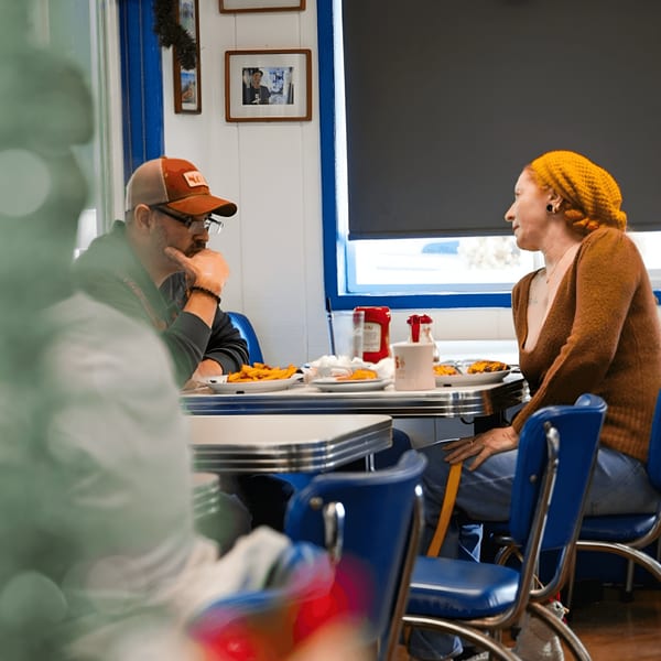 Two patrons enjoying diner food at Eat at Joe's, with blue booths and classic diner tables.