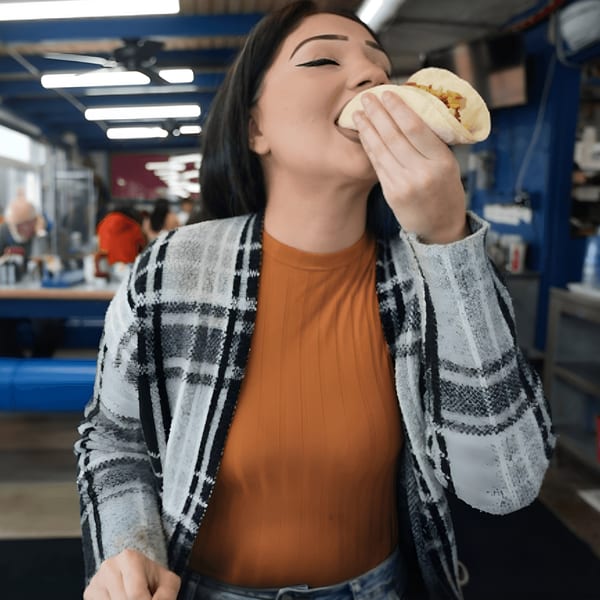A woman in a diner takes a bite of a taco, with a blurred background of the restaurant.