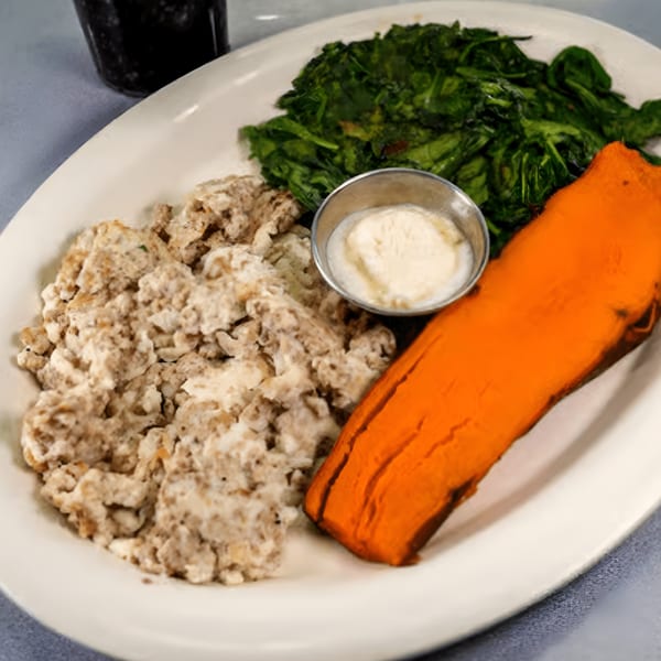 A diner plate with scrambled eggs, a side of spinach, and a sweet potato, with a small cup of sauce.