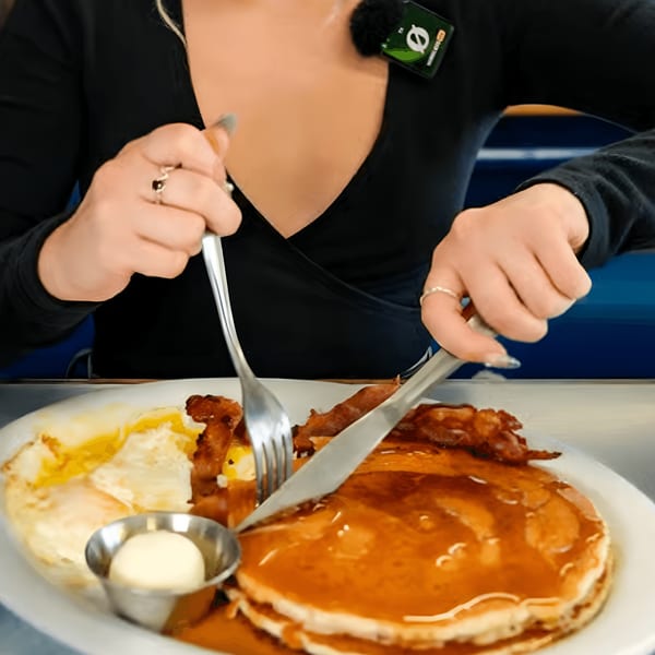 A person cutting into a stack of pancakes with bacon and eggs at Eat at Joe's diner.