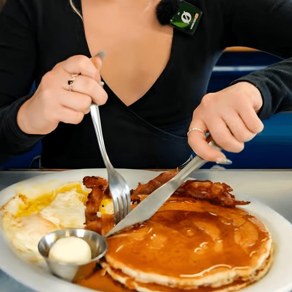 A person cutting into a stack of pancakes with bacon and eggs at Eat at Joe's diner.