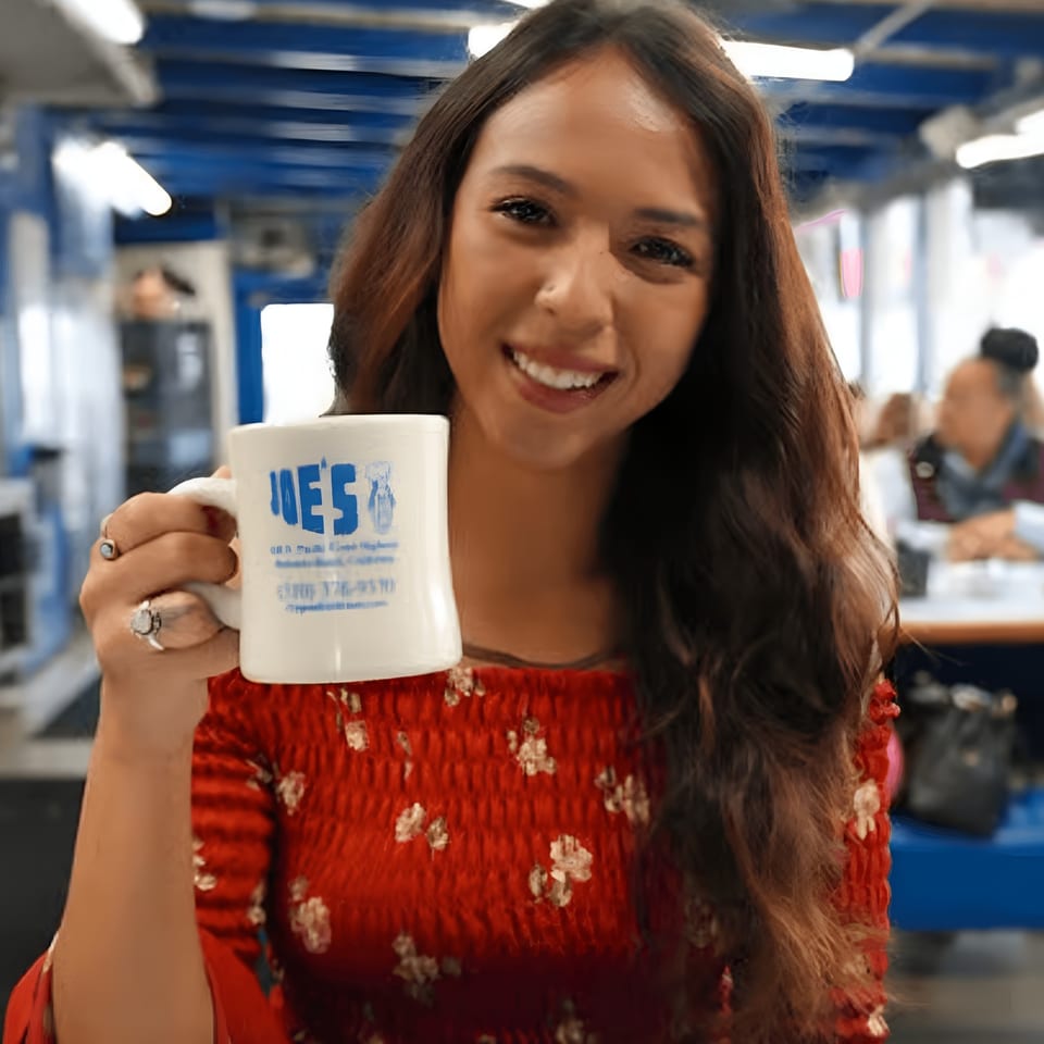 Smiling woman in a red dress holding a white "Eat at Joe's" diner mug.