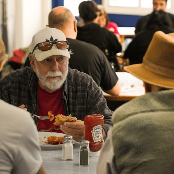A man in a white cap and plaid shirt eats a diner meal with ketchup, salt, and pepper shakers.