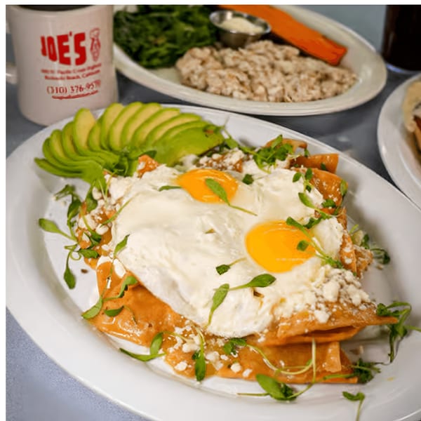 Chilaquiles with two fried eggs, avocado, and microgreens, with a Joe's diner coffee mug.