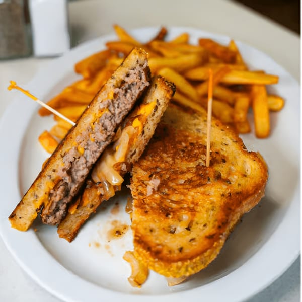 A patty melt with melted cheese and grilled onions, served with a side of french fries.